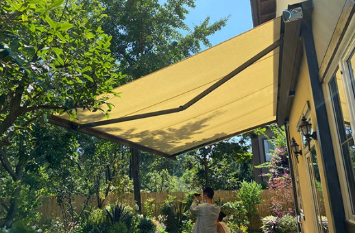 Wall-mounted beige retractable folding arm awning extended over a residential garden patio