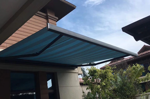 Blue striped wall-mounted retractable folding arm awning extended over a residential patio