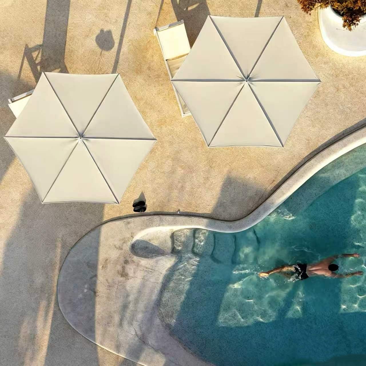Overhead view of two white Milan patio umbrellas providing shade beside a residential swimming pool