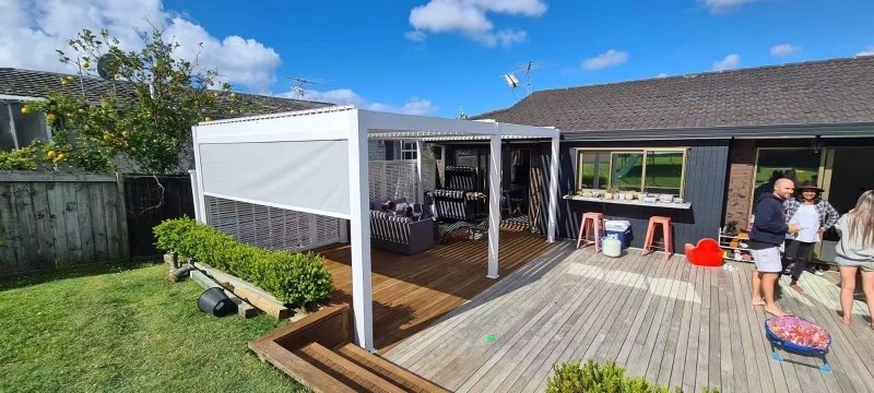 White aluminum patio pergola with a retractable windproof side screen installed over a residential backyard deck