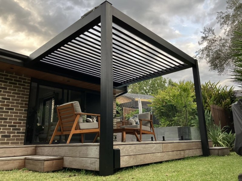 Black aluminum louvered pergola installed over a residential garden patio with adjustable roof slats